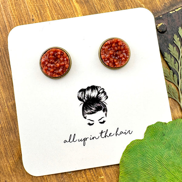 All Up In The Hair | Online Accessory Boutique Located in Mooresville, NC | Two rust colored druzies set in a bronze earring setting. The earrings are on a white, All Up In The Hair branded packaging card. The card is laying on a wood background, alongside green leaves.