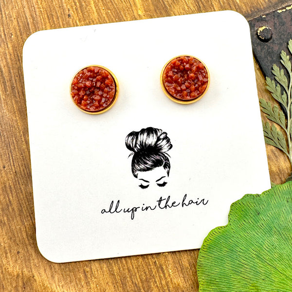 All Up In The Hair | Online Accessory Boutique Located in Mooresville, NC | Two rust colored druzies set in a gold earring setting. The earrings are on a white, All Up In The Hair branded packaging card. The card is laying on a wood background, alongside green leaves.