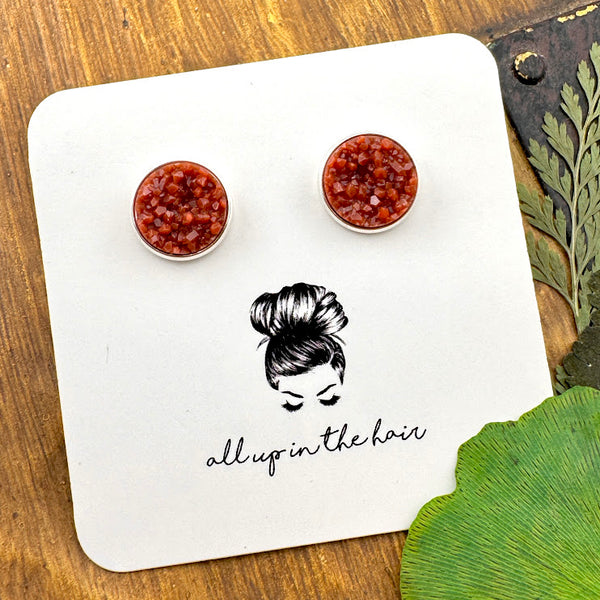 All Up In The Hair | Online Accessory Boutique Located in Mooresville, NC | Two rust colored druzies set in a silver earring setting. The earrings are on a white, All Up In The Hair branded packaging card. The card is laying on a wood background, alongside green leaves.