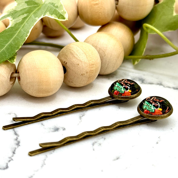 All Up In The Hair | Online Accessory Boutique Located in Mooresville, NC | Side view of two Sink Or Swim Bobby Pins laying on a white marble background with a wood bead garland and ivy leaves.