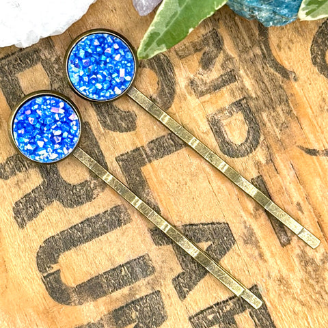 All Up In The Hair | Online Accessory Boutique Located in Mooresville, NC | Two Sky Blue Druzy Bobby Pins on a wood background with black lettering. There are crystals and ivy leaves at the top of the image.