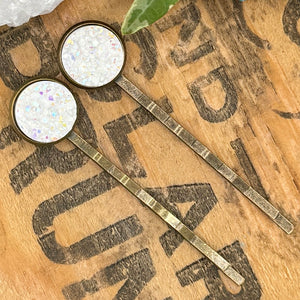 All Up In The Hair | Online Accessory Boutique Located in Mooresville, NC | Two white druzy bobby pins laying on a grey background surrounded by colorful glitter.