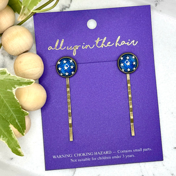 All Up In The Hair | Online Accessory Boutique Located in Mooresville, NC | Two Star Bobby Pins on an indigo colored, All Up In The Hair branded packaging card. The card is laying on a white marble background alongside a wood bead garland and ivy leaves.