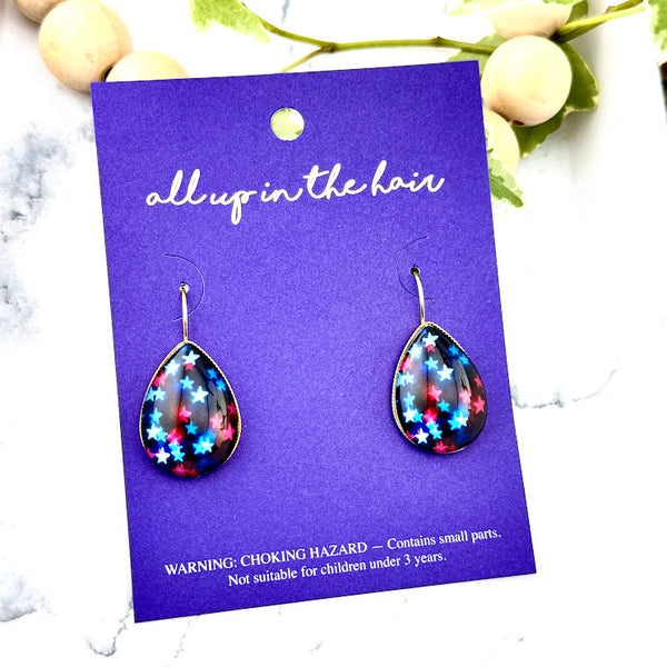 All Up In The Hair | Online Accessory Boutique Located in Mooresville, NC | Two Star Teardrop Earrings on an indigo, colored, All Up In The Hair branded packaging card. The card is laying on a white marble background.