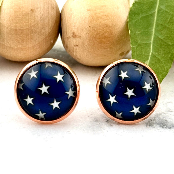 All Up In The Hair | Online Accessory Boutique Located in Mooresville, NC | Two round earrings with a blue background and white stars laying on a white marble background. There is a wood bead garland and ivy leaves behind the earrings.