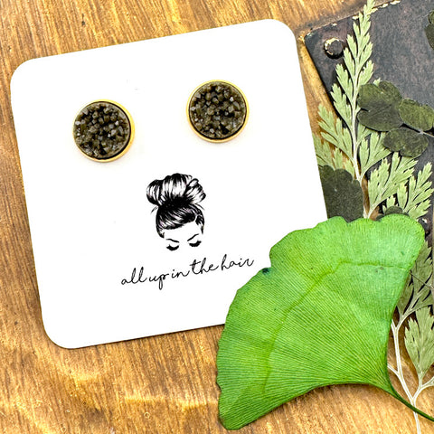 All Up In The Hair | Online Accessory Boutique Located in Mooresville, NC | Two dark grey druzies set in gold settings. The earrings are on a white, All Up In The Hair branded packaging card. The card is laying on a wood background alongside green leaves.