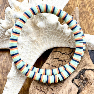 All Up In The Hair | Online Accessory Boutique Located in Mooresville, NC | Two blue, brown, yellow, and mint heishi bracelets laying on a piece of driftwood and a sunflower.