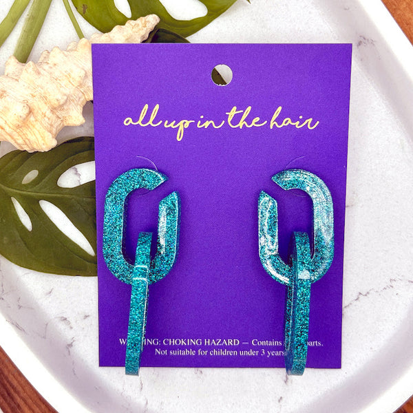 All Up In The Hair | Online Accessory Boutique Located in Mooresville, NC | Two Teal Chain Earrings on an indigo backer card. The card is laying on two monstera leaves on a white marble background.