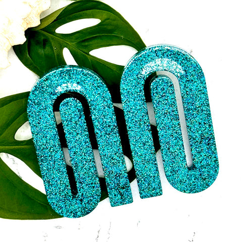 All Up In The Hair | Online Accessory Boutique Located in Mooresville, NC | Two Teal Paperclip Earrings laying on two monstera leaves on a white background.