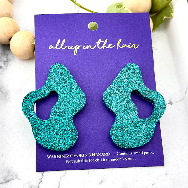 All Up In The Hair | Online Accessory Boutique Located in Mooresville, NC | Two Teal Wave Earrings on an indigo colored, All Up In The Hair branded packaging card. The card is laying on a white marble background.