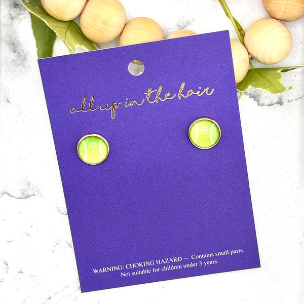 All Up In The Hair | Online Accessory Boutique Located in Mooresville, NC | Two Tennis Ball Earrings on an indigo colored, All Up In The Hair branded packaging card. The card is laying on a white marble background alongside a wood bead garland and ivy leaves.