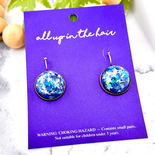 All Up In The Hair | Online Accessory Boutique Located in Mooresville, NC | Two Titan Dangle Earrings on an indigo colored, All Up In The Hair branded packaging card. The card is laying on a white marble background.