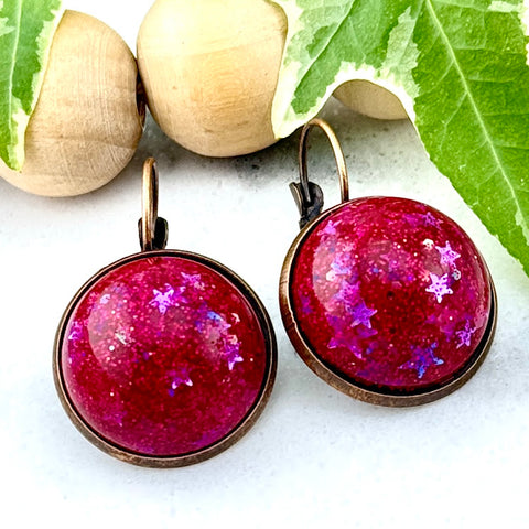 All Up In The Hair | Online Accessory Boutique Located in Mooresville, NC | Two Dark Pink Dangle Earrings on a white marble background. Behind the earrings is a wood bead garland and ivy leaves.