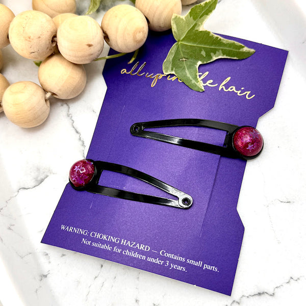 All Up In The Hair | Online Accessory Boutique Located in Mooresville, NC | Two Vega Snap Clips on an indigo colored, All Up In The Hair branded packaging card. The card is laying on a white marble background. At the top of the image is a wood bead garland and ivy leaves.