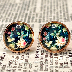 All Up In The Hair | Online Accessory Boutique Located in Mooresville, NC | Close up of our Vintage Floral Earrings. The earrings are dark blue with a peach, vintage, rose print. The earrings are laying on a book page.