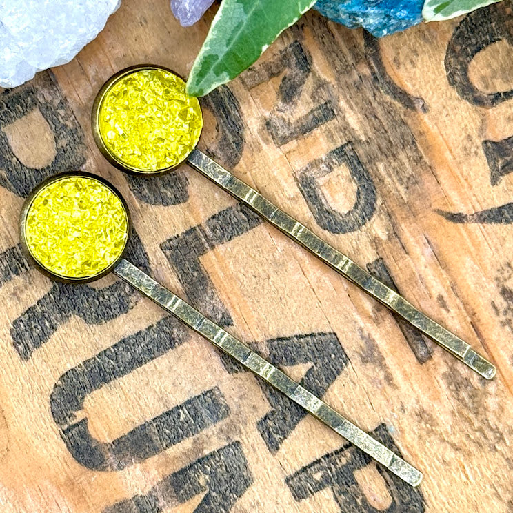 All Up In The Hair | Online Accessory Boutique Located in Mooresville, NC | Two bright yellow druzy bobby pins laying on a grey background, surrounded by colorful confetti.