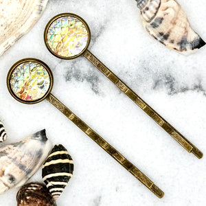 All Up In The Hair | Online Accessory Boutique Located in Mooresville, NC | Two Yellow Mermaid Bobby Pins laying on a white marble background surrounded by shells.