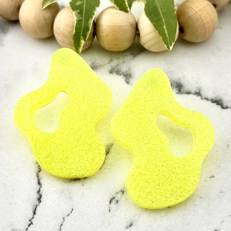 All Up In The Hair | Online Accessory Boutique Located in Mooresville, NC | Two Yellow Wave Earrings on a white marble background. There is a wood bead garland and ivy leaves behind the earrings.