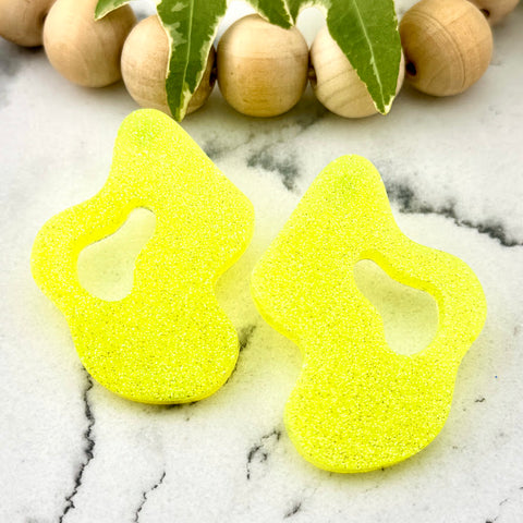 All Up In The Hair | Online Accessory Boutique Located in Mooresville, NC | Two Yellow Wave Earrings on a white marble background. There is a wood bead garland and ivy leaves behind the earrings.
