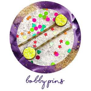 All Up In The Hair | Online Accessory Boutique Located in Mooresville, NC | Purple and gold circle outline surrounding an image of two neon yellow druzy bobby pins, surrounded by colorful glitter