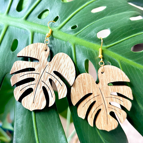 All Up In The Hair | Online Accessory Boutique Located in Mooresville, NC | Two wood monstera leaf earrings hanging on a large green monstera leaf.