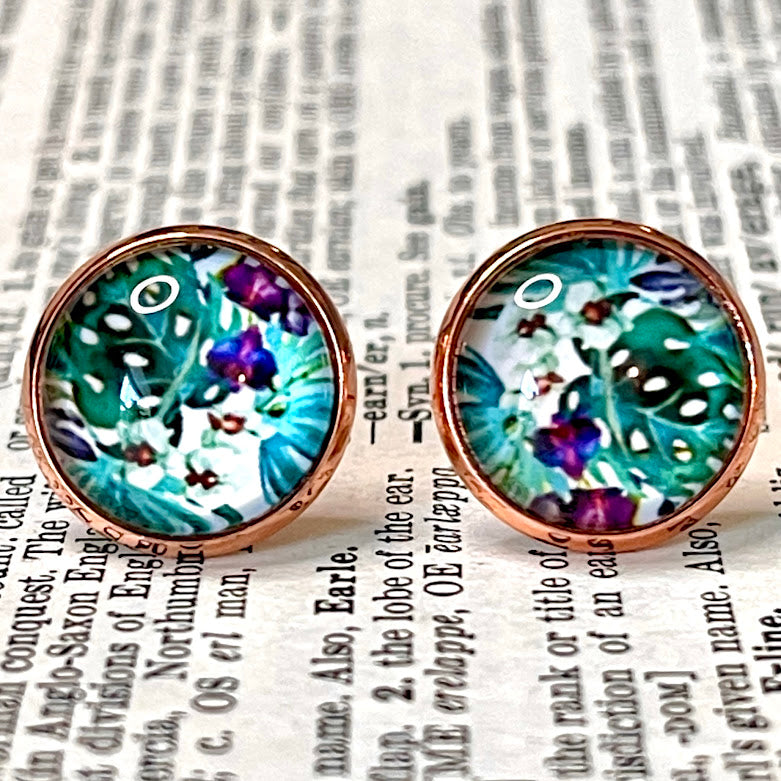 All Up In The Hair | Online Accessory Boutique Located in Mooresville, NC | Close up of two earrings on a book page. The earrings feature a cabochon with tropical foliage and orchids. The cabochon is set in a rose gold colored setting.