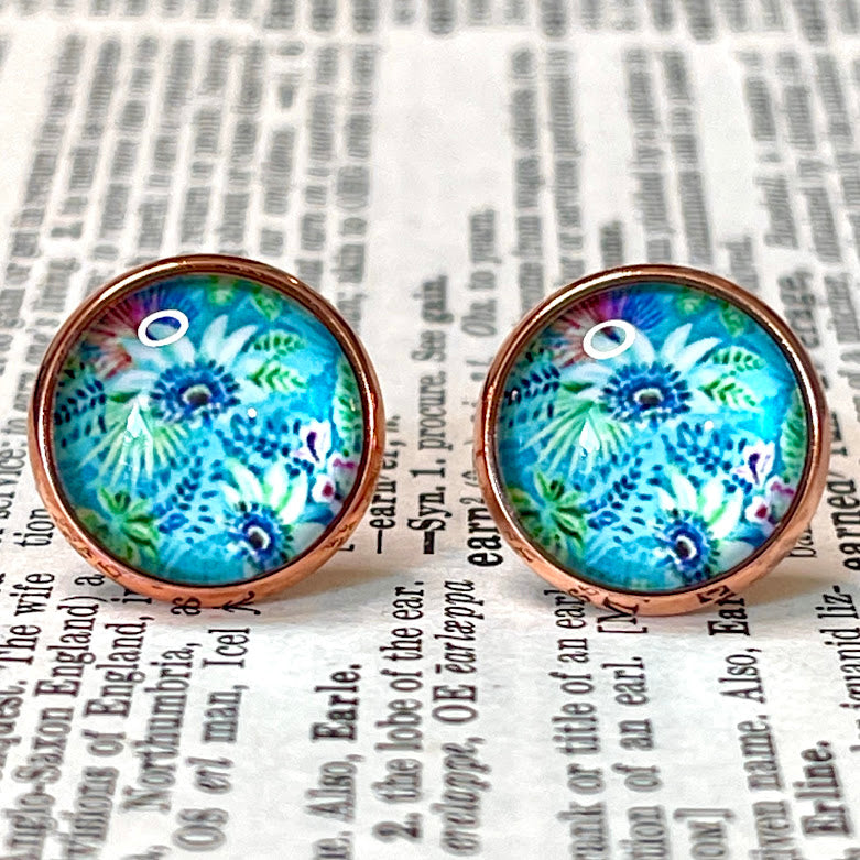 All Up In The Hair | Online Accessory Boutique Located in Mooresville, NC | Close up of two blue earrings with brilliantly colored tropical flowers. The earrings are laying on a book page.