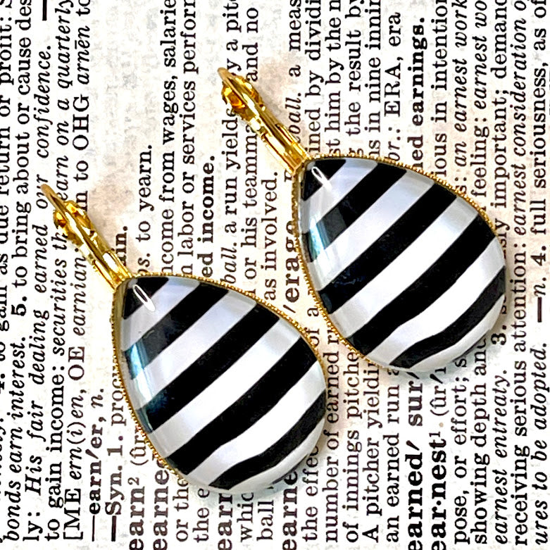 All Up In The Hair | Online Accessory Boutique Located in Mooresville, NC | Two black and white stripe teardrop earrings in a gold setting laying on a book page.